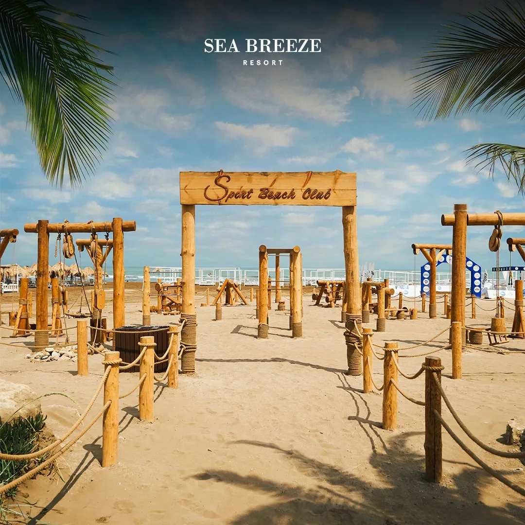 Деревянная вывеска Sport Beach Club и тренажёры на песке у пляжной спортивной зоны